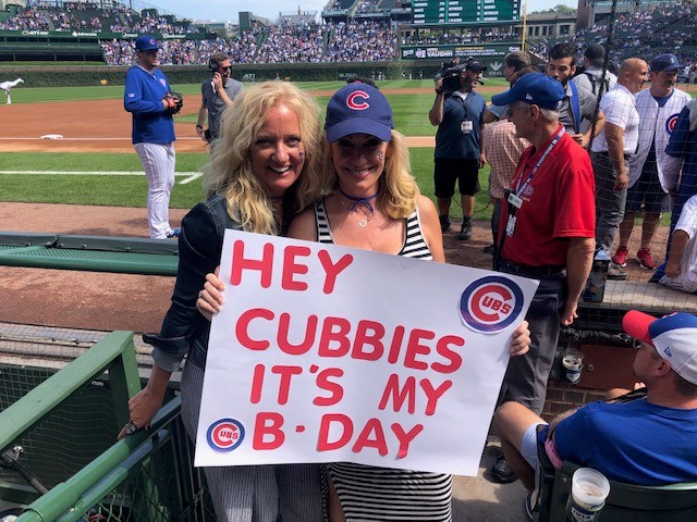 Two women at baseball game holding up sign