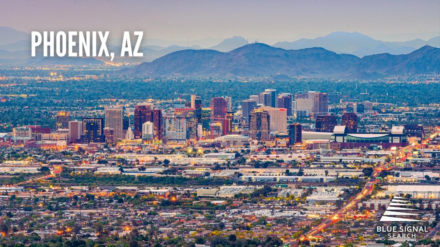 Aerial view of downtown Phoenix, AZ, at dusk, surrounded by desert mountains.