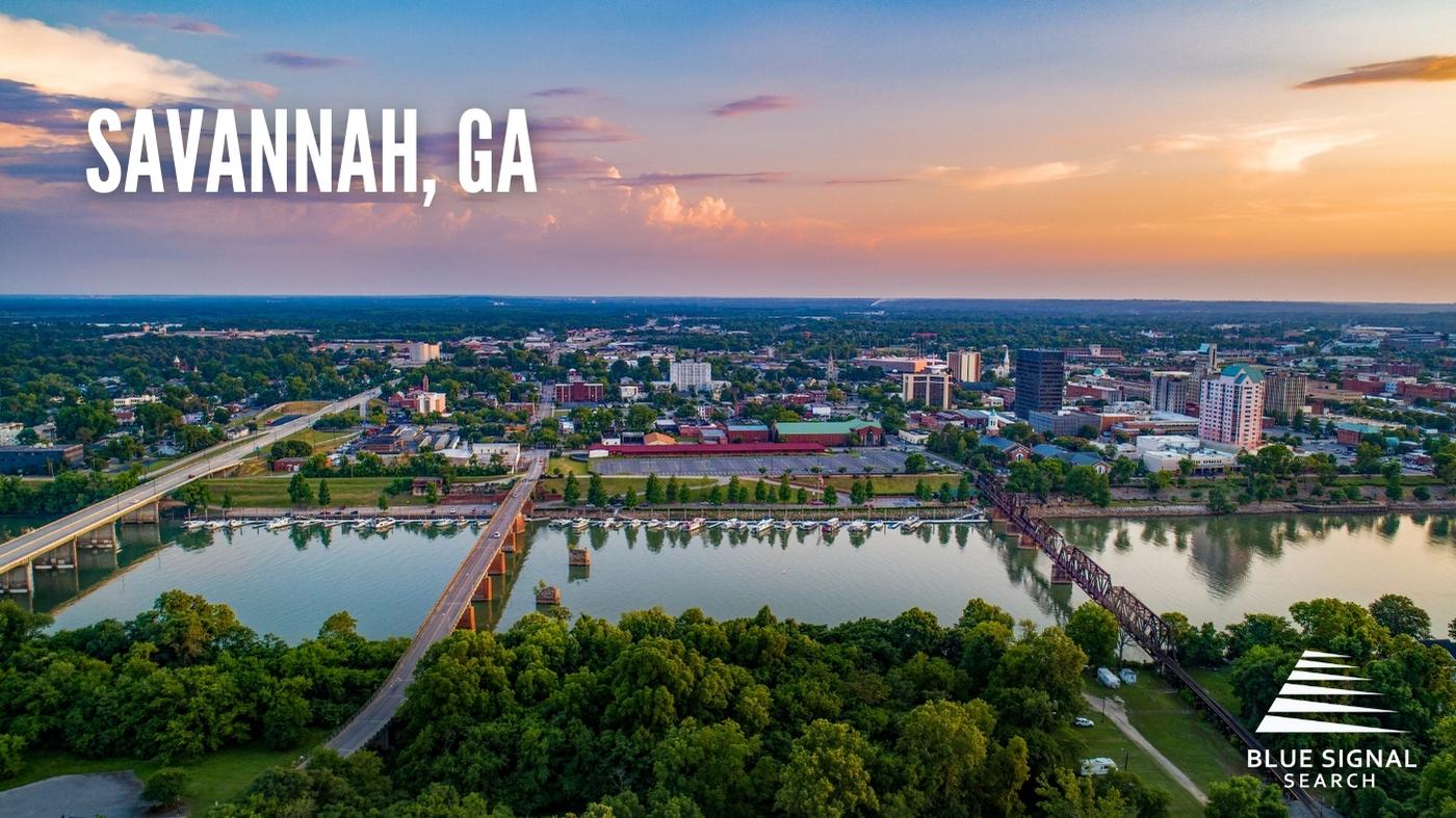 Aerial view of downtown Savannah, GA, at sunset with a river and bridges in the foreground.