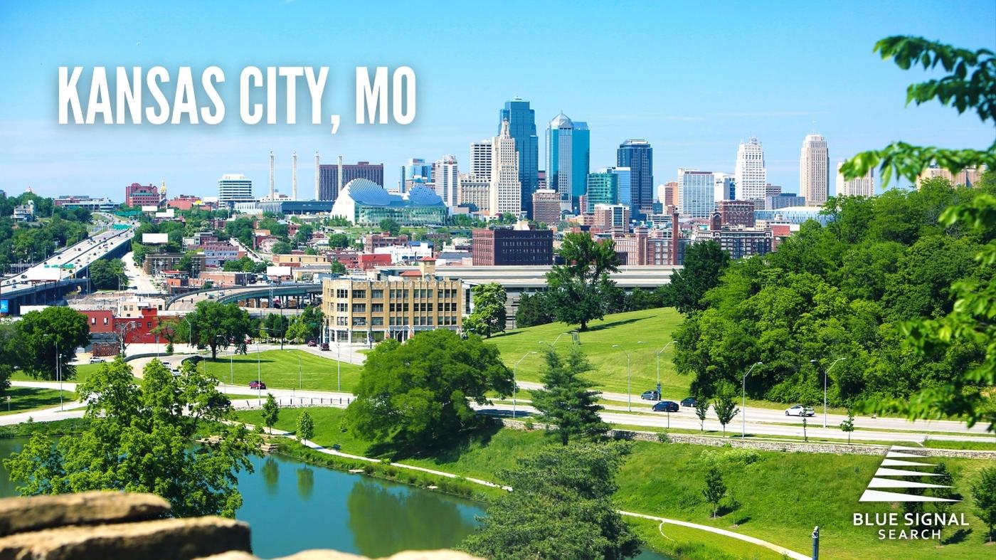 Aerial view of downtown Kansas City, MO, with a river and green parkland in the foreground.