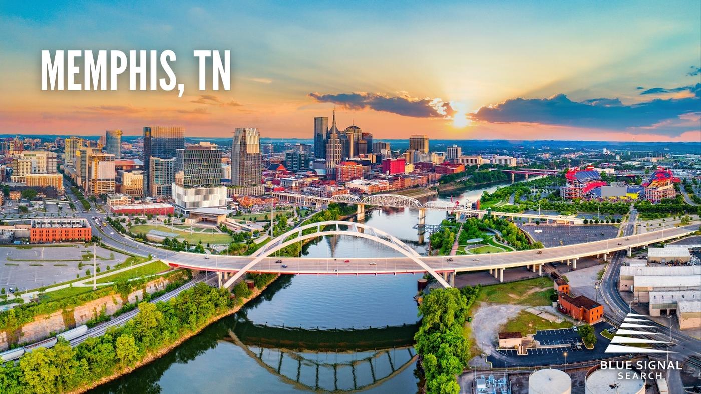 Aerial view of downtown Memphis, TN, with a prominent bridge crossing a river at sunset.