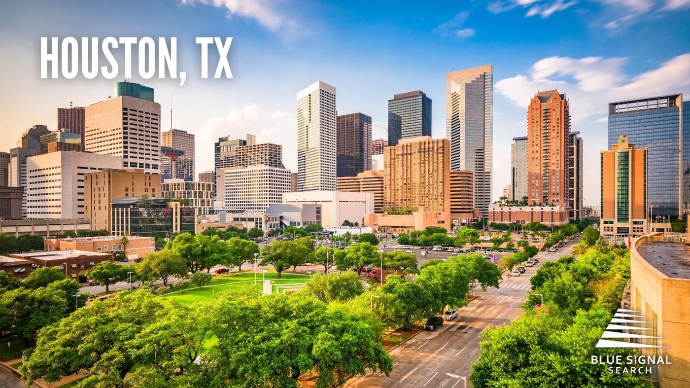 Aerial view of downtown Houston, TX, with skyscrapers and lush greenery in the foreground.