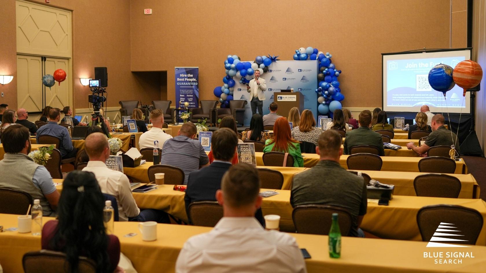 Speaker presenting to Blue Signal Summit 2024 attendees in a conference room with space-themed decor.