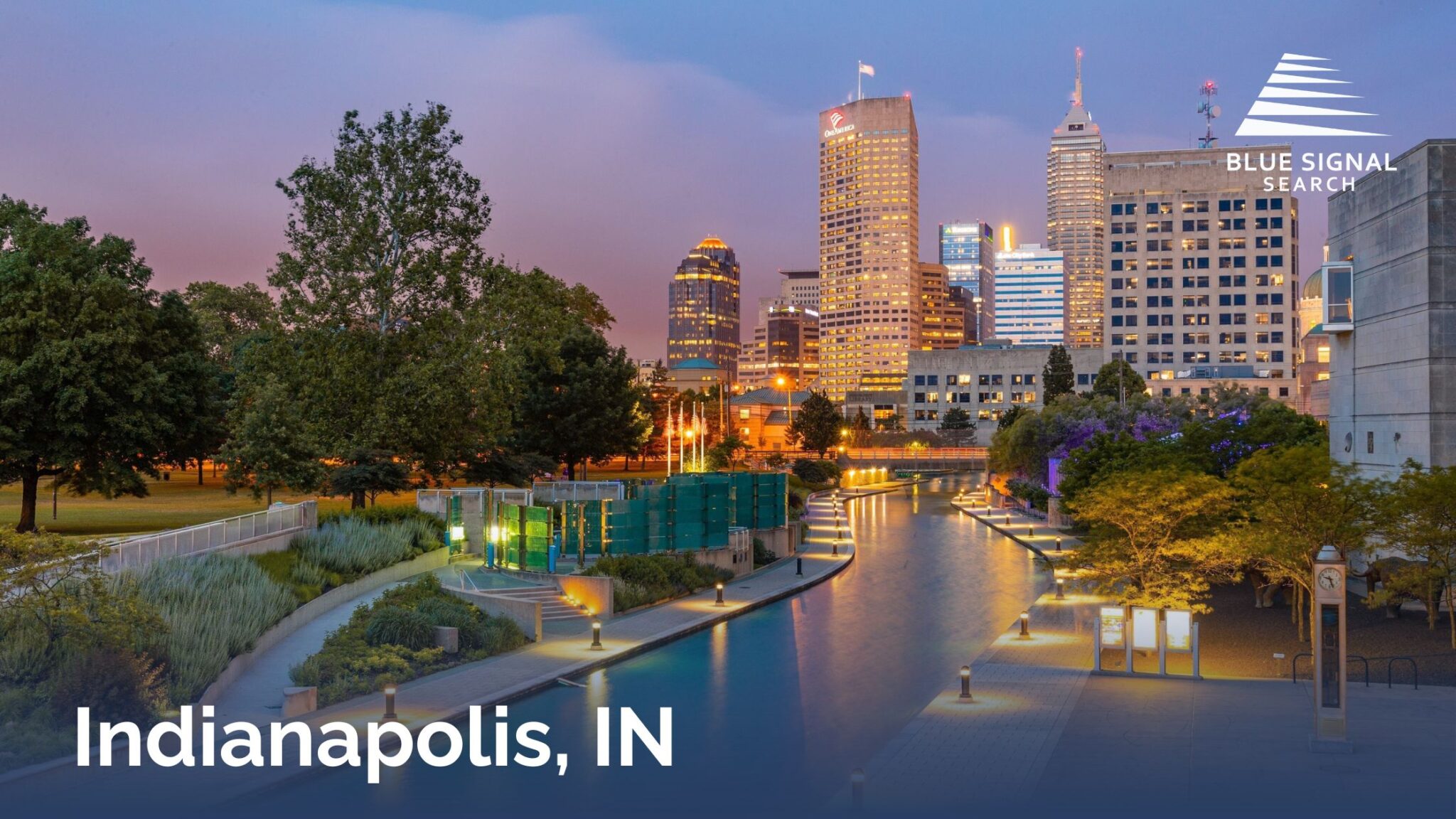 Downtown Indianapolis skyline with canal walk and illuminated city buildings at dusk.